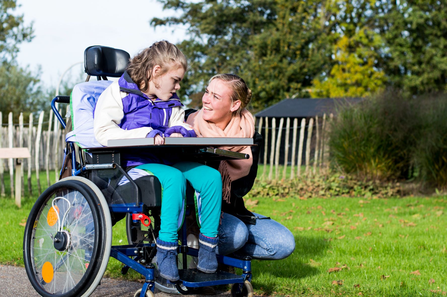 A woman kneels down next to a young girl in a wheelchair