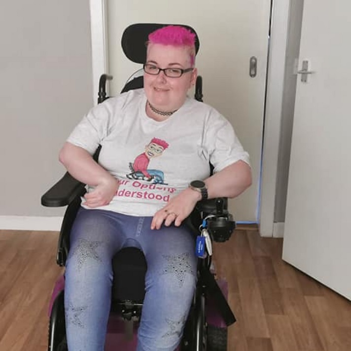 Danielle, a woman with pink hair in a wheelchair. She is wearing a T shirt with a cartoon of herself on it
