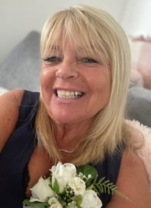 A smiling woman with blonde hair holds a bouquet of flowers