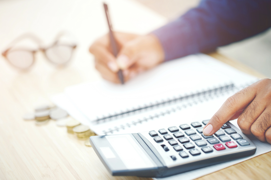 A man uses a calculator and writes in a notebook with the other hand