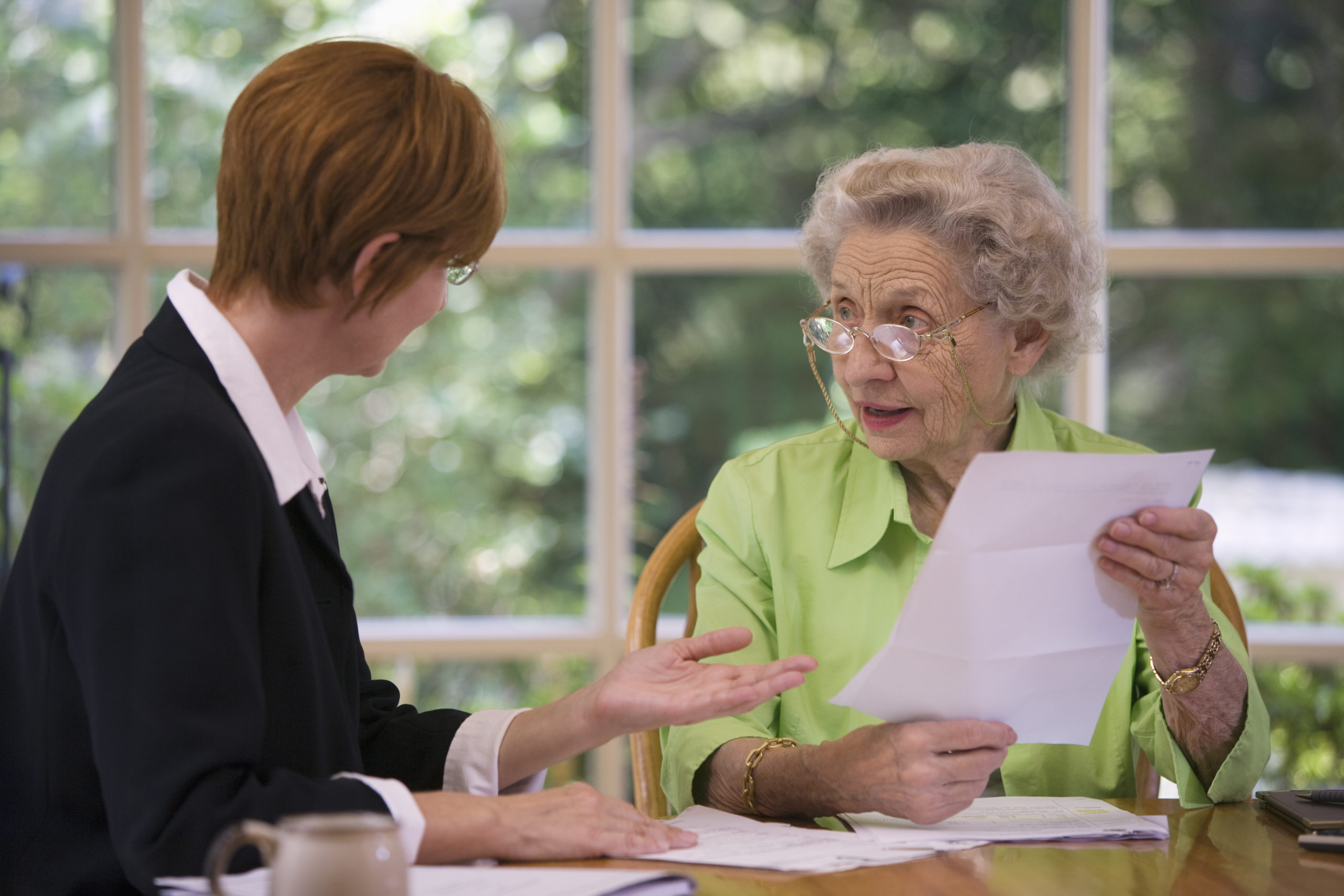 An elderly woman holds a piece of paperwork while another woman explains something to her