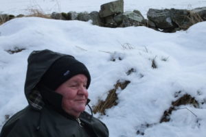 A man wearing a winter coat and hat is pictured against a snowy backdrop