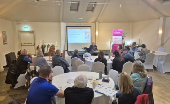 Attendees present at the Help to Build a Disabled People's Organisation in Argyll and Bute event, sitting round tables listening to Donald Macleod, SDSS CEO, speaking